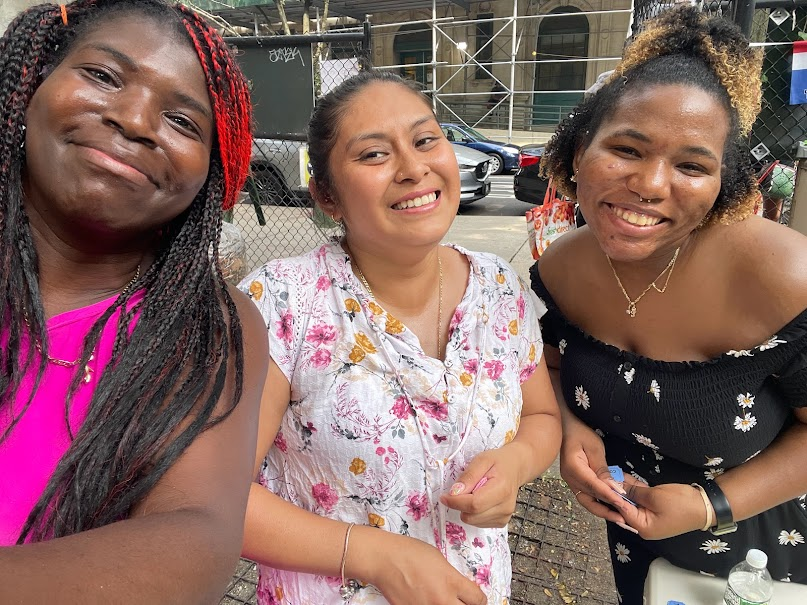 Three women smiling together during a community distribution event